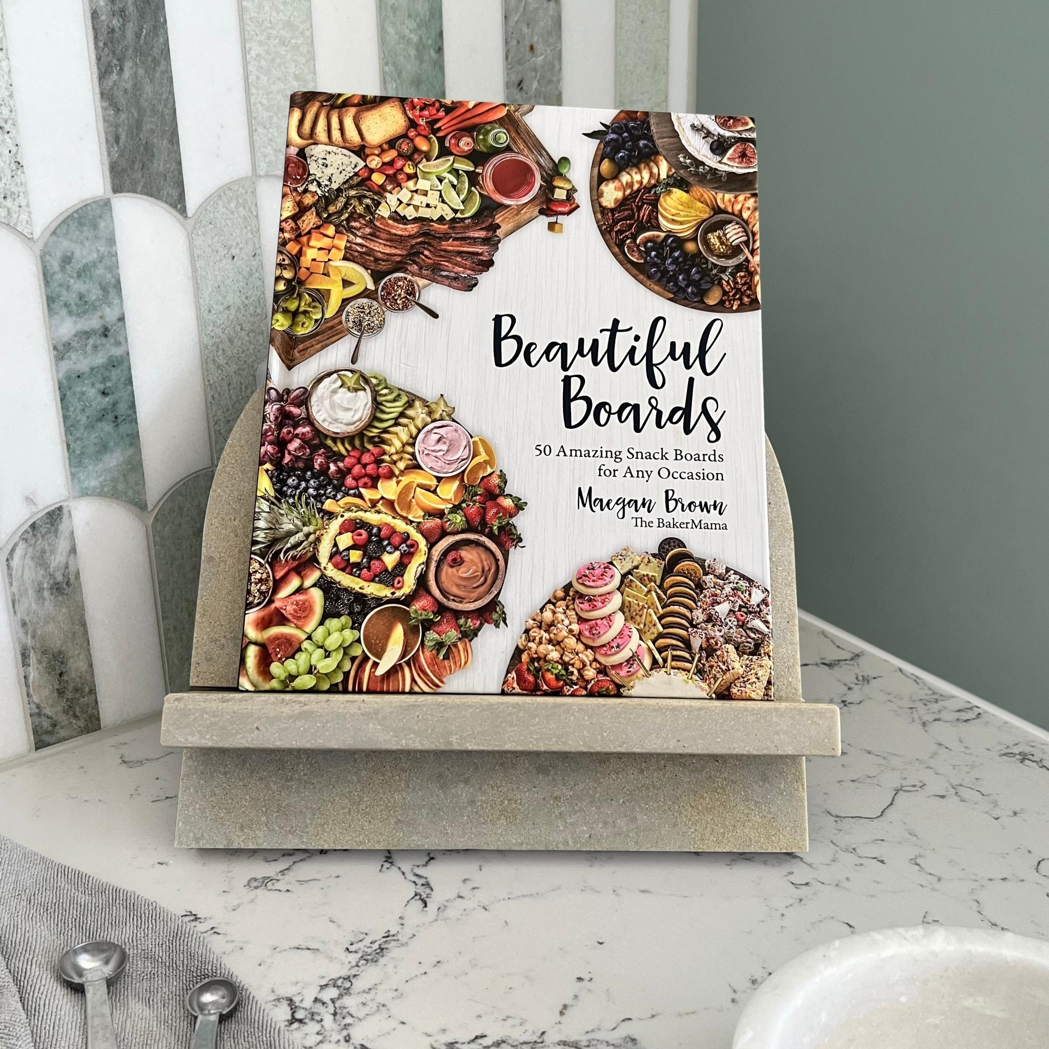 Stone Cookbook Stand in Caesarstone Primordia. Made from quality marble like material. Arch shape. Shown with Beautiful Boards Cookbook - The BakerMama - Maegan Brown.