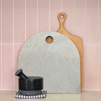 Large concrete look arch serving platter with timber paddle board and black pestle and mortar. Pastel pink tiled splashback. Caesarstone Primordia,
