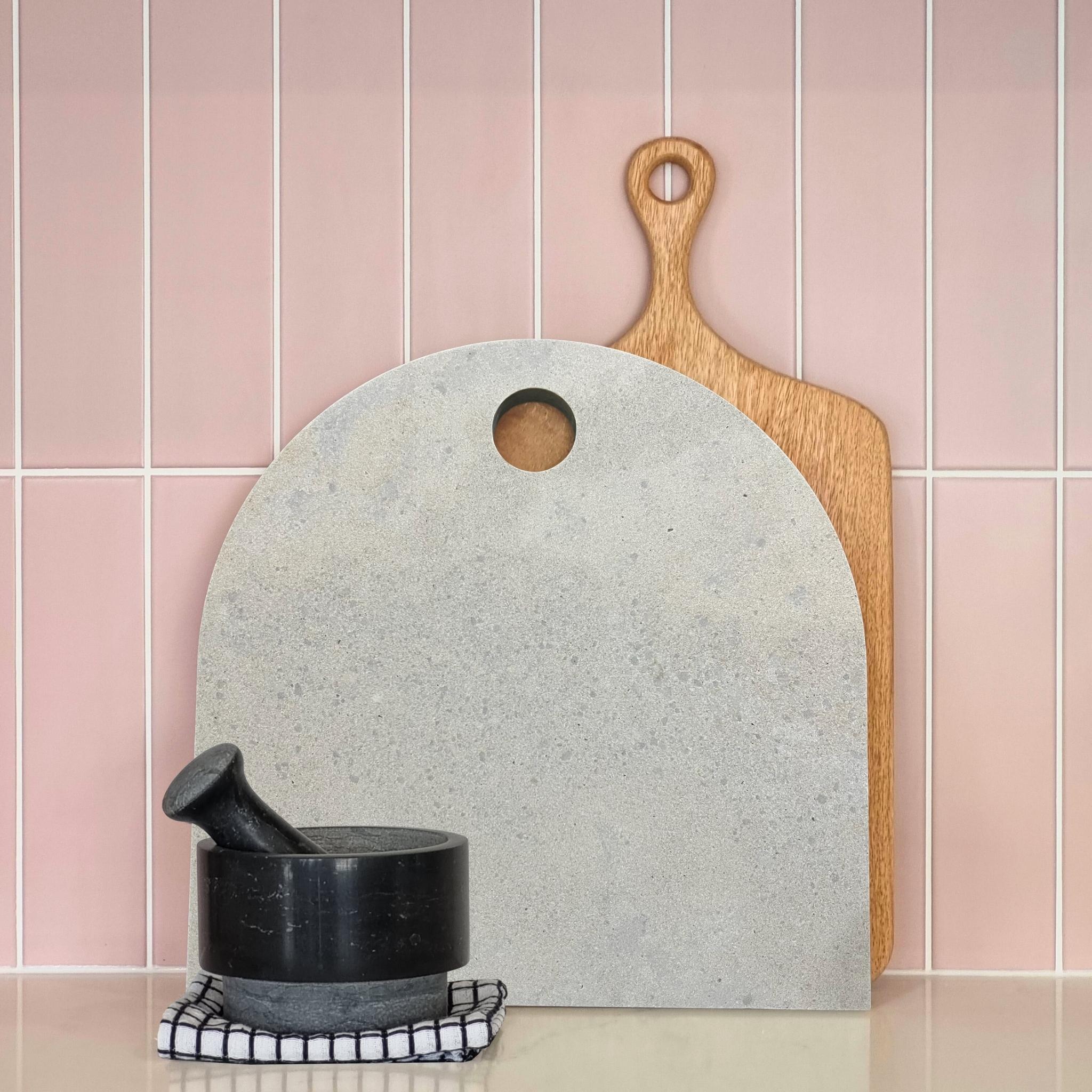 Large concrete look arch serving platter with timber paddle board and black pestle and mortar. Pastel pink tiled splashback. Caesarstone Primordia,