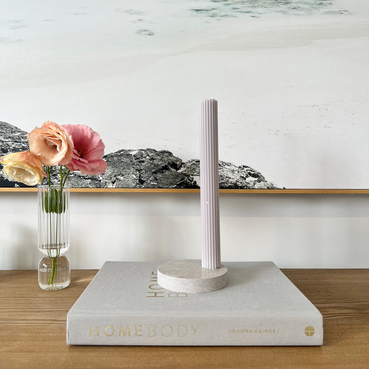 Quartz Round Single Candle Holder in Caesarstone Clamshell created by Aureliia Collection. Styled with navy ridge pillar candle and vase with flowers on timber table. This candle holder has a beautiful fusion of light grey with white features, underscored by drifting veins on a neutral base. The perfect home decor item.