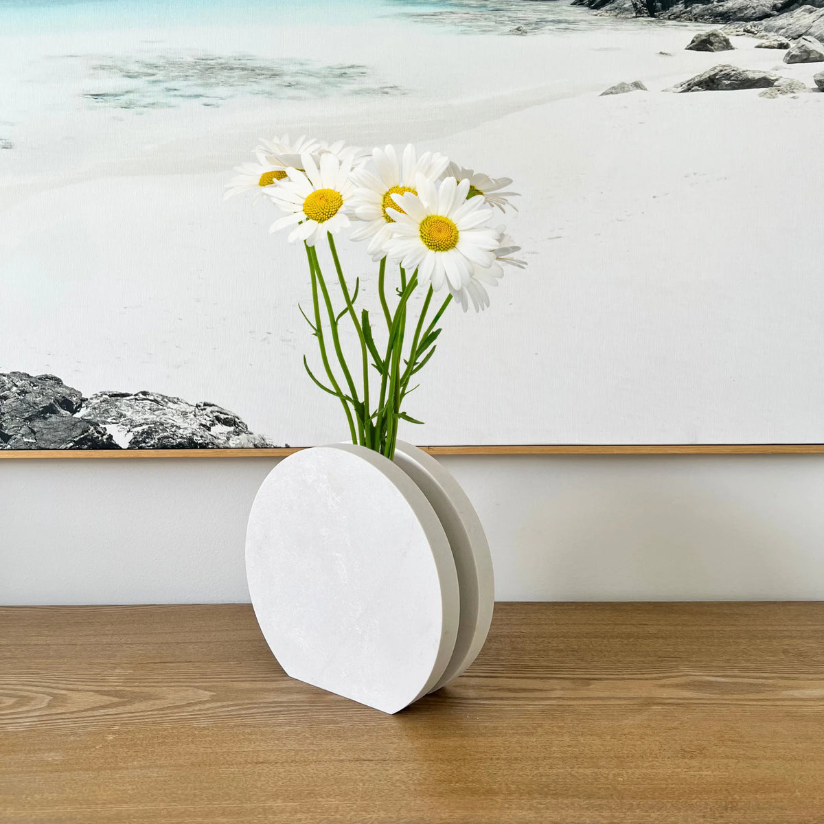 Image of Round Vase used to display daisies, a timeless display piece. Crafted from durable stone, evoking a luxurious contemporary feel. Available in Cloudburst Concrete by Caesarstone - soft swells of pure white that veil a solid, creamy base, for an infinitely beautiful surface. An ideal decorative accent.
