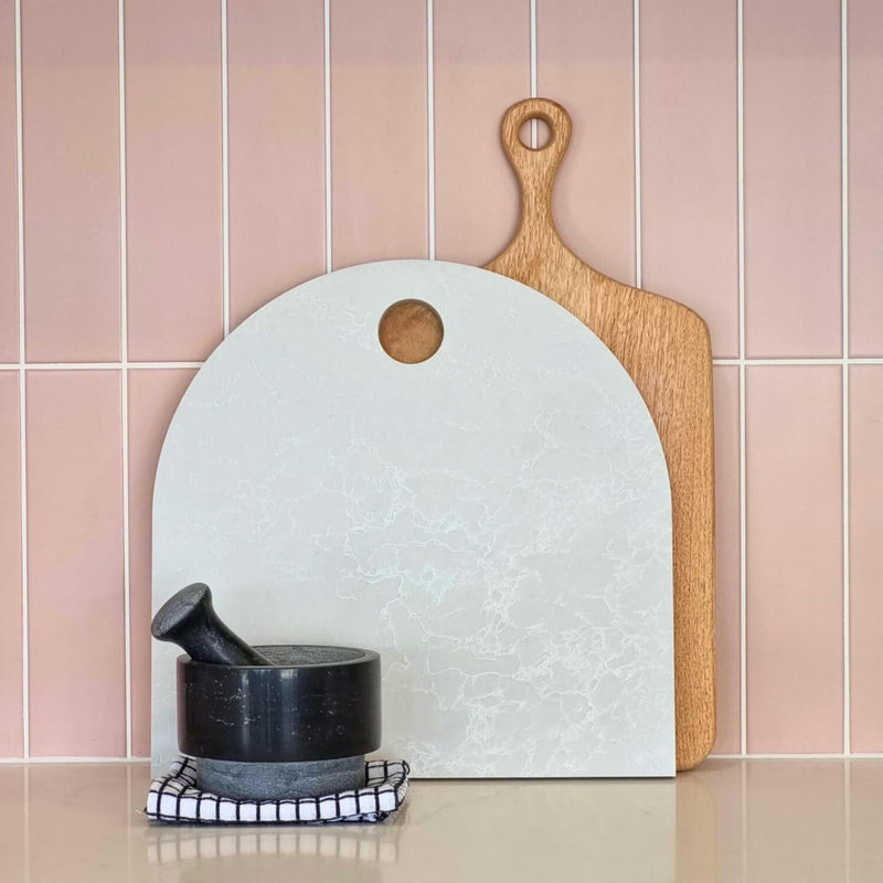 Large marble arch serving platter with timber paddle board and black pestle and mortar. Pastel pink tiled splashback. Caesarstone Alpine Mist.