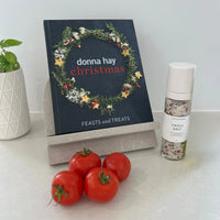 Donna Hay Christmas cookbook with tomatoes and a bottle of Tasteology Chilli Salt on a stone cookbook stand.