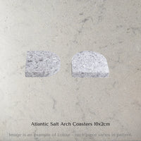 Two Caesarstone Atlantic Salt Arch Coasters on a concrete surface with text 'Atlantic Salt Arch Coasters 10x2cm'.