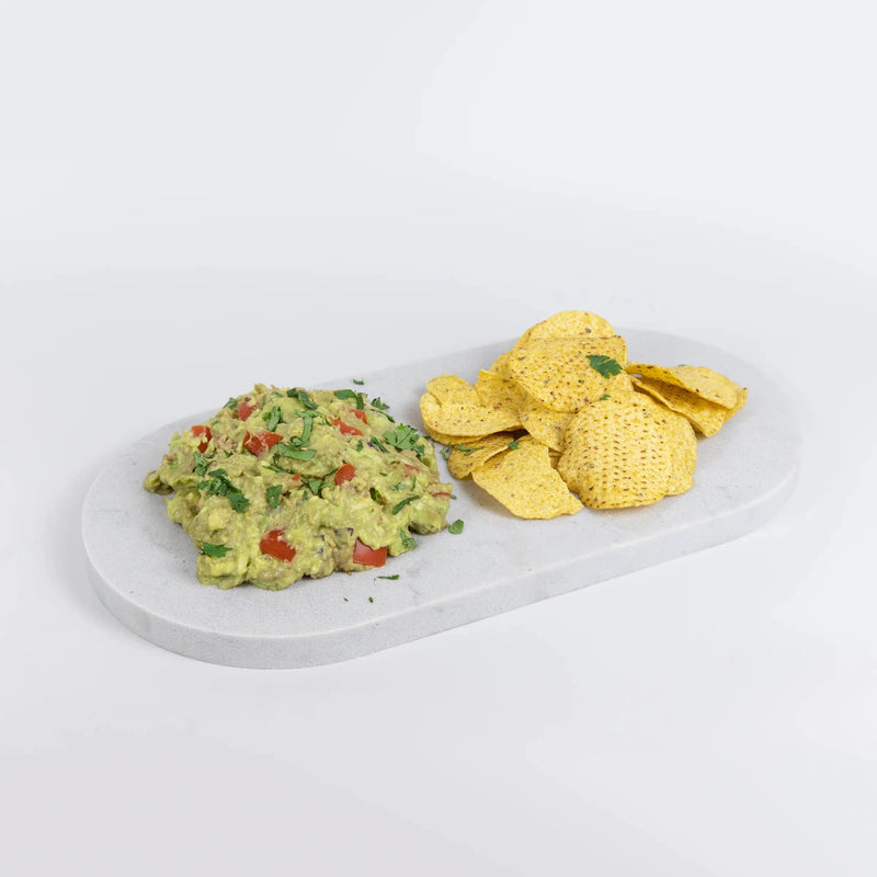 Guacamole with tortilla chips on a marble platter against a light gray background. Caesarstone Georgian Bluffs by Aureliia Collection.