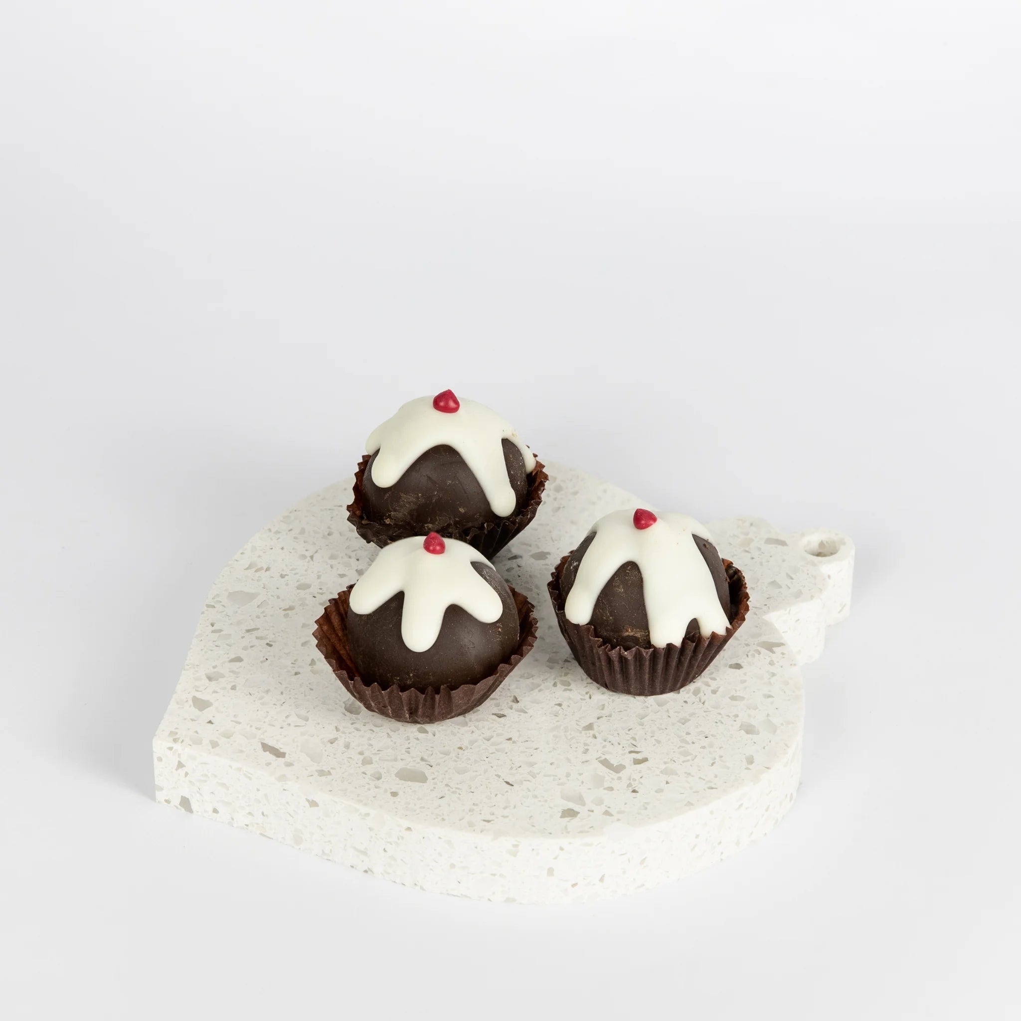Three chocolate truffles with white icing and red toppings on a stone coaster.
