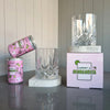 Two cans of Curatif Tommy's Margarita and two DStill unbreakable glasses on a Caesarstone White Attica marble coasters on reflective surface with a striped wall background.