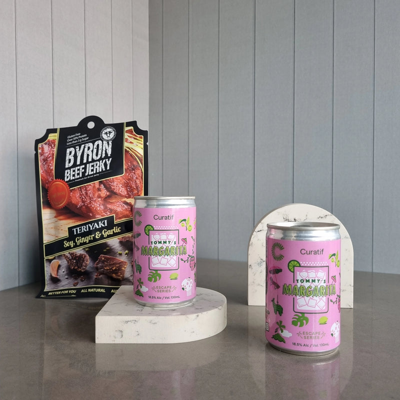 Two cans of Tommy's Mangos on a stand with a box of Byron Beef Jerky in the background.