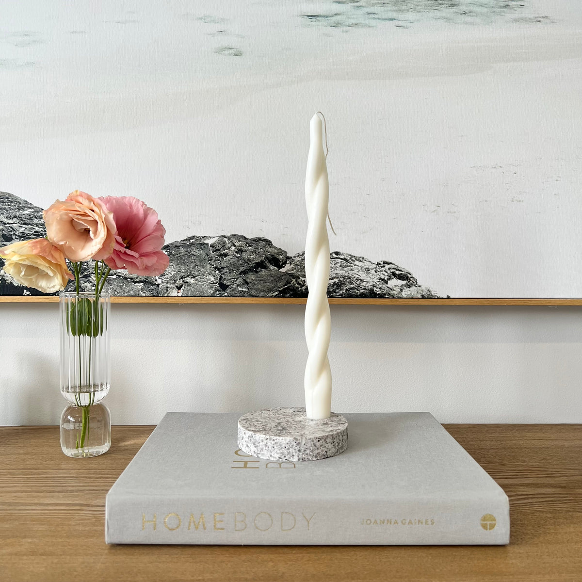 Quartz Round Single Candle Holder in Caesarstone Atlantic Salt created by Aureliia Collection. Styled Studio McKenna Chunky Twist Taper pillar candle and vase with flowers on timber table. This candle holder has a light grey base peppered with whites, browns, and blacks, in a mix that conjures the purity of unrefined sea salts. The perfect home decor item.