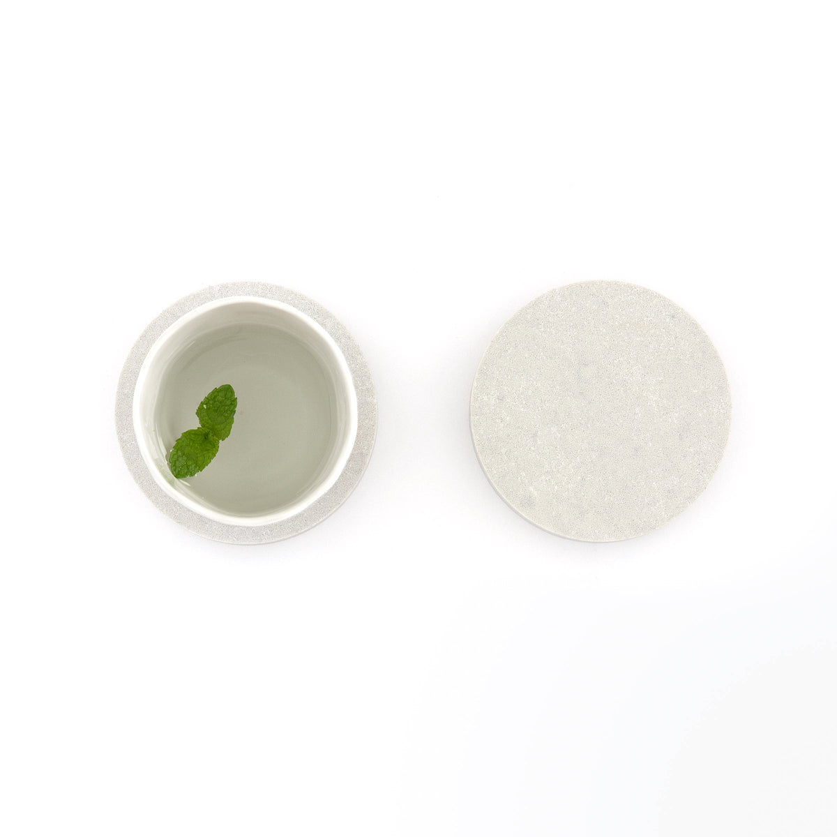 Round quartz coasters in Caesarstone Airy Concrete™ created by Aureliia Collection. Similar to a marble, the Round Quartz Coasters shown with glass of water, featuring mint leaf. An excellent home decor gift for someone who has it all.