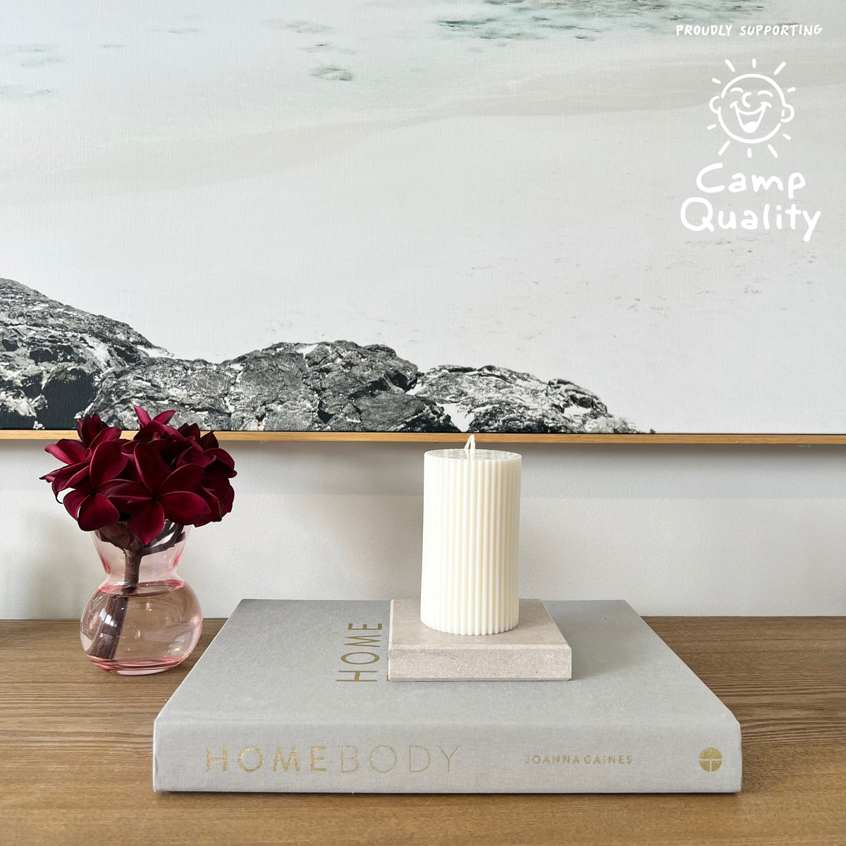 Square Candle Holder in Caesarstone Topus Concrete created by Aureliia Collection. Styled with Studio McKenna white pillar candle, upon Joanna Gaines book  next to vase with fresh flowers on timber table. This candle holder has full of movement, opacity, and depth of delicate mineral formations over a warm greige base, flushed with rugged patinas and pastel-pink undertones. The perfect home decor item.