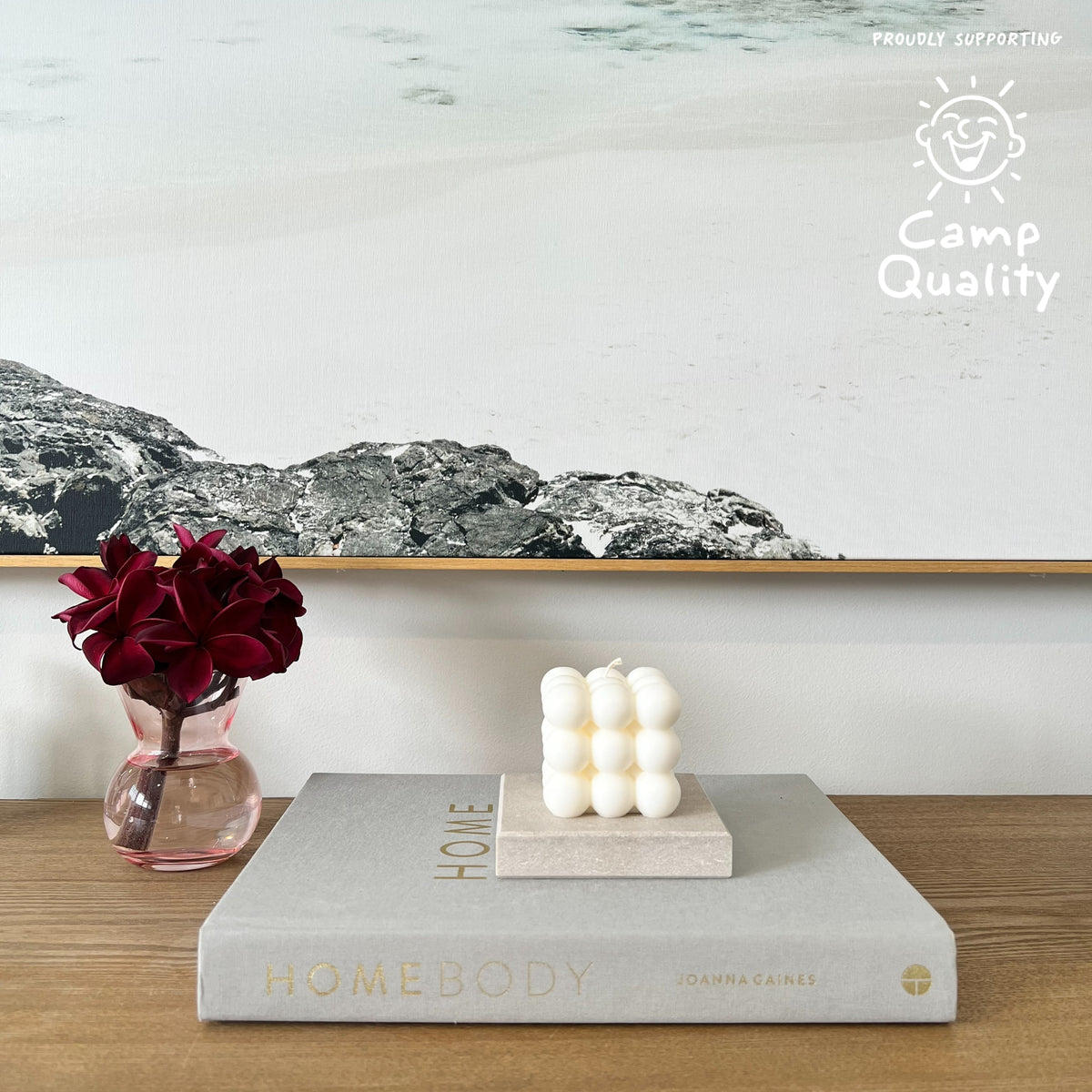 Square Stone Candle Holder in Caesarstone Topus Concrete created by Aureliia Collection. Styled with Studio McKenna No. 27 candle, upon Joanna Gaines book  next to vase with fresh flowers on timber table. This candle holder has full of movement, opacity, and depth of delicate mineral formations over a warm greige base, flushed with rugged patinas and pastel-pink undertones. The perfect home decor item.